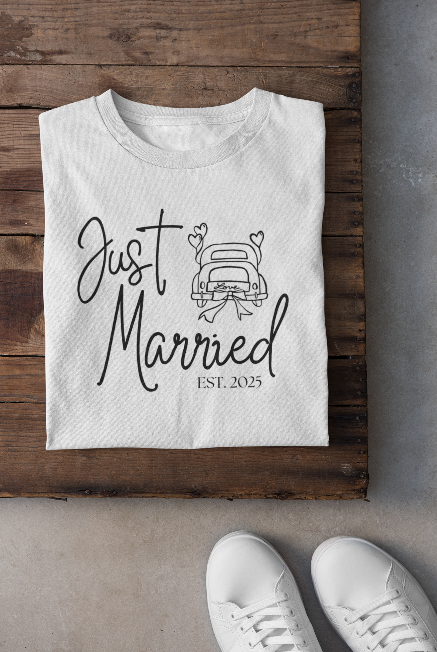 White t-shirt with 'Just Married Est. 2025' text and car graphic on a wooden surface.
